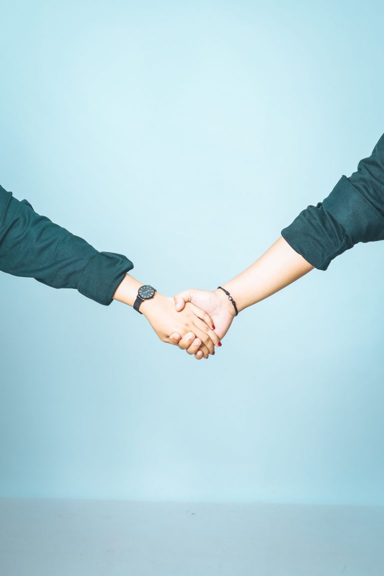 Close-up of two people shaking hands against a blue background, signifying agreement and partnership.