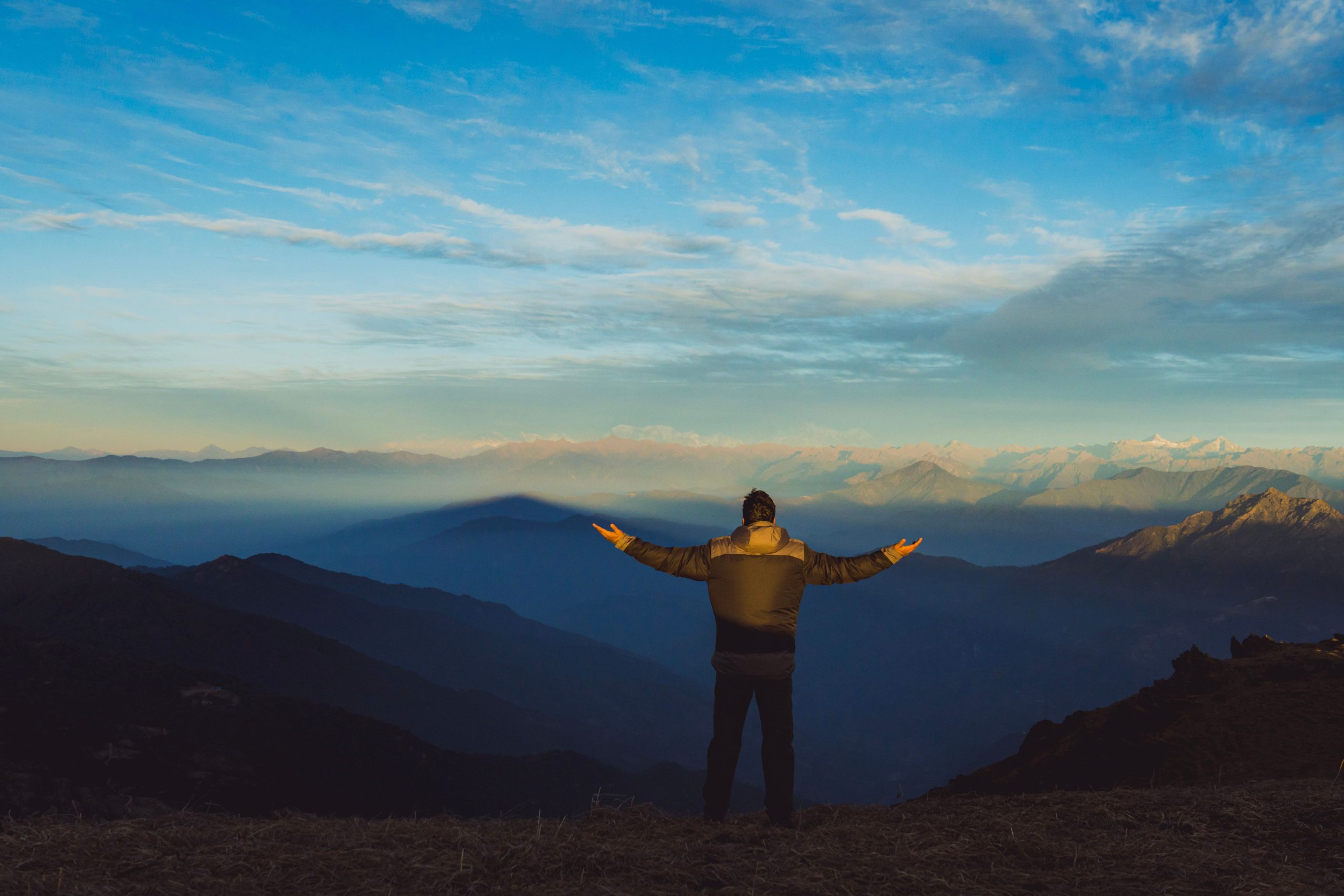 A man stands on a mountain ridge with arms outstretched, embracing the sunrise view.