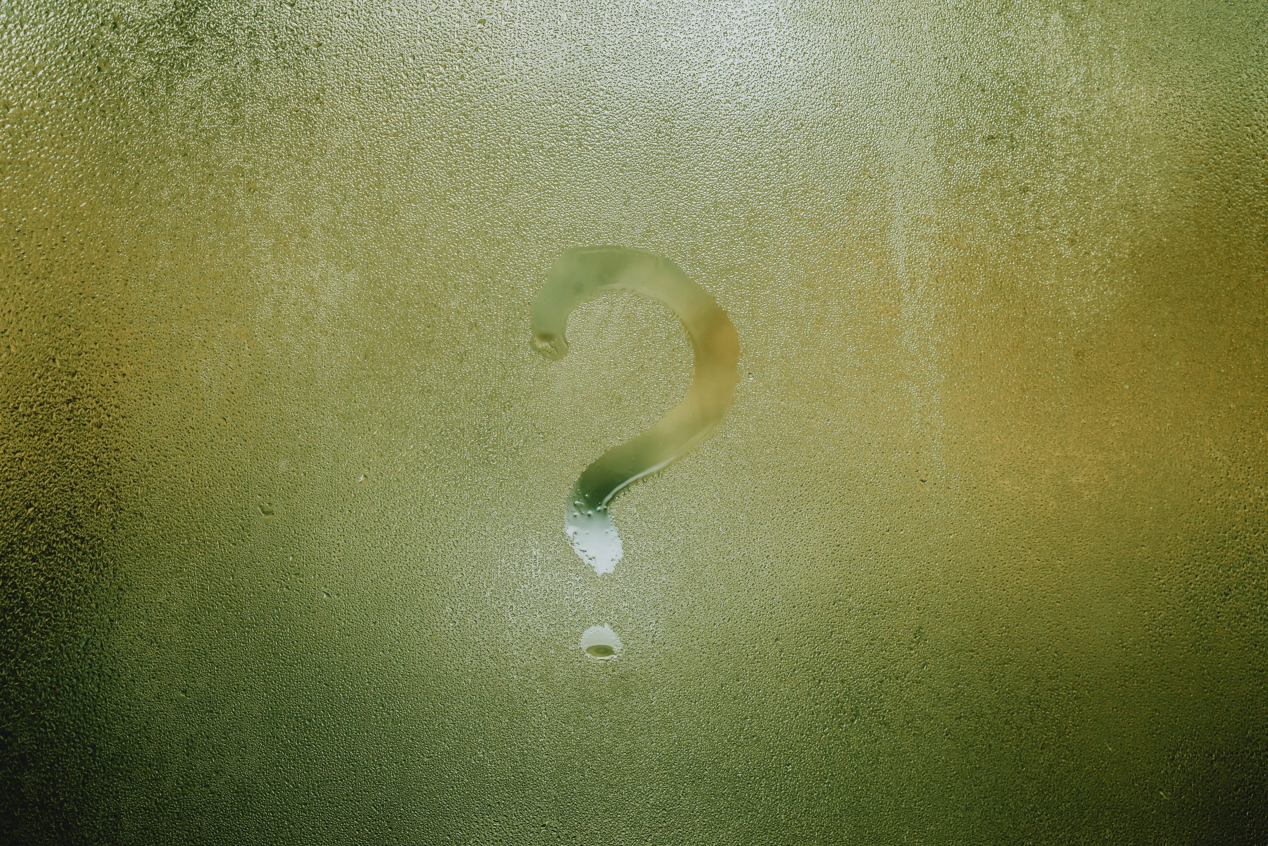 Translucent wet glass window covered with water drops with question mark on surface